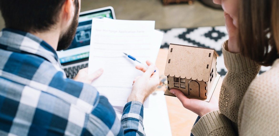Image of a couple holding a cardboard house while working out Inheritance Tax to support a new article from Jameson and Partners Estate Agents about the amount of Inheritance tax paid by Altrincham residents being in the Top 10 nationally