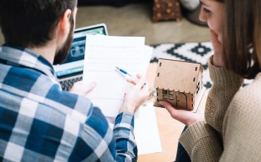 Image of a couple holding a cardboard house while working out Inheritance Tax to support a new article from Jameson and Partners Estate Agents about the amount of Inheritance tax paid by Altrincham residents being in the Top 10 nationally