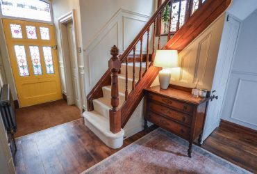 An image of a hallway showing front door, carpeted stairs and a lit lamp on a bureau for the Property Sales page of Jameson and Partners Altrincham estate agents website